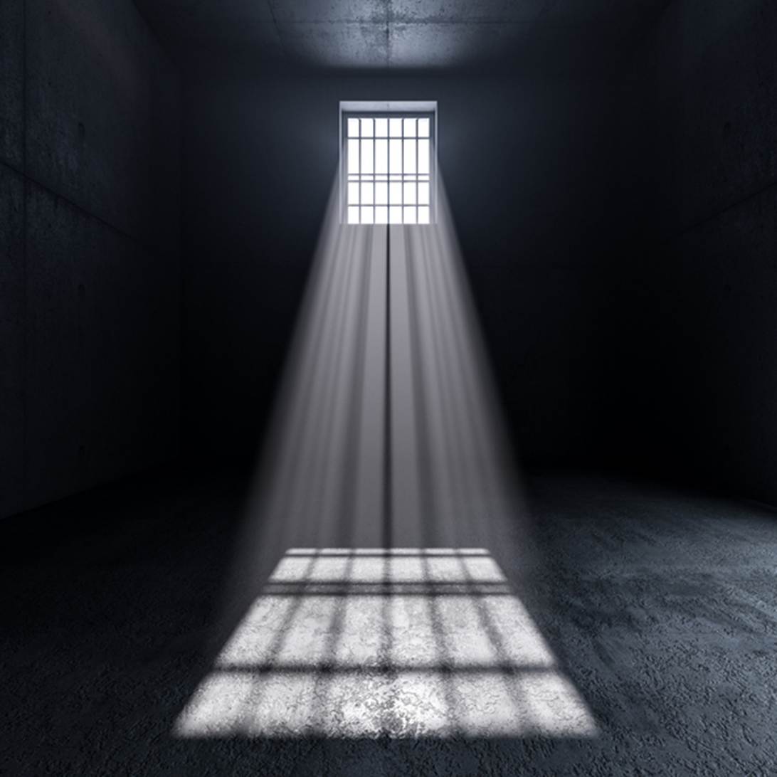 A dark prison cell with a barred window and light shining through. The image illustrates content about wrongful arrest and false imprisonment.